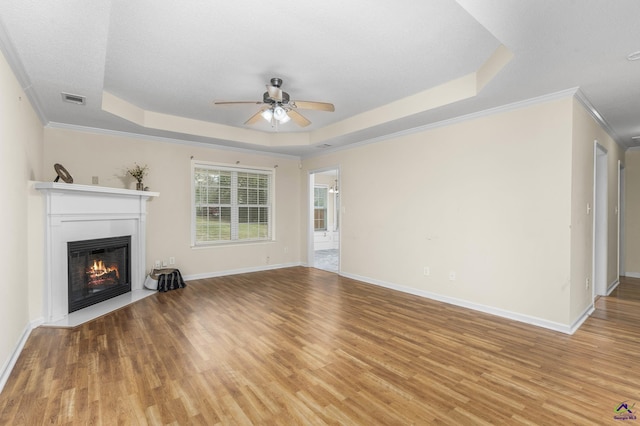 unfurnished living room featuring visible vents, baseboards, light wood-type flooring, a lit fireplace, and a raised ceiling