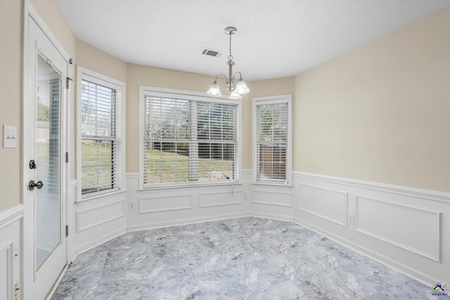 unfurnished dining area with an inviting chandelier, a healthy amount of sunlight, visible vents, and a textured ceiling