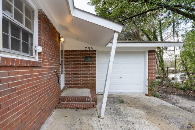 view of exterior entry featuring brick siding, concrete driveway, an attached garage, and fence