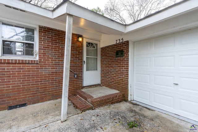 doorway to property with visible vents, driveway, an attached garage, crawl space, and brick siding