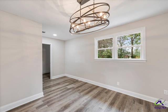 empty room featuring a notable chandelier, recessed lighting, wood finished floors, and baseboards