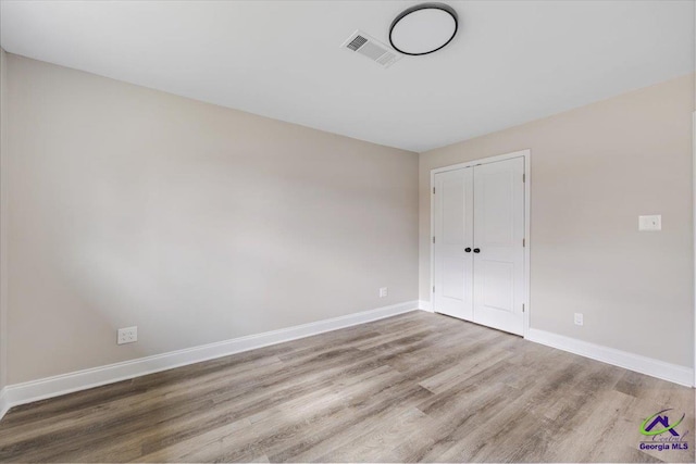 unfurnished bedroom featuring visible vents, wood finished floors, baseboards, and a closet