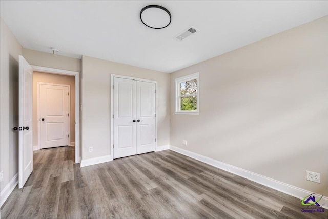 unfurnished bedroom with visible vents, baseboards, a closet, and wood finished floors