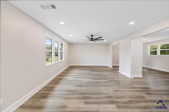 empty room featuring visible vents, plenty of natural light, baseboards, and wood finished floors