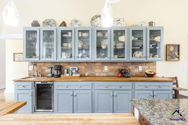 bar with backsplash, beverage cooler, pendant lighting, indoor wet bar, and a sink