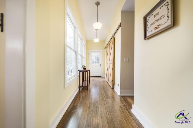 corridor featuring dark wood finished floors, baseboards, and a barn door