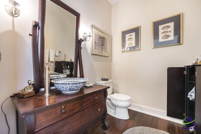 bathroom featuring baseboards, toilet, wood finished floors, and vanity