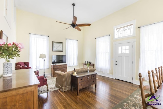 living area with baseboards, a ceiling fan, and dark wood-style flooring