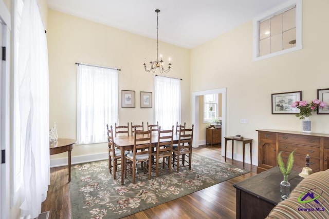 dining room featuring an inviting chandelier, wood finished floors, baseboards, and a towering ceiling