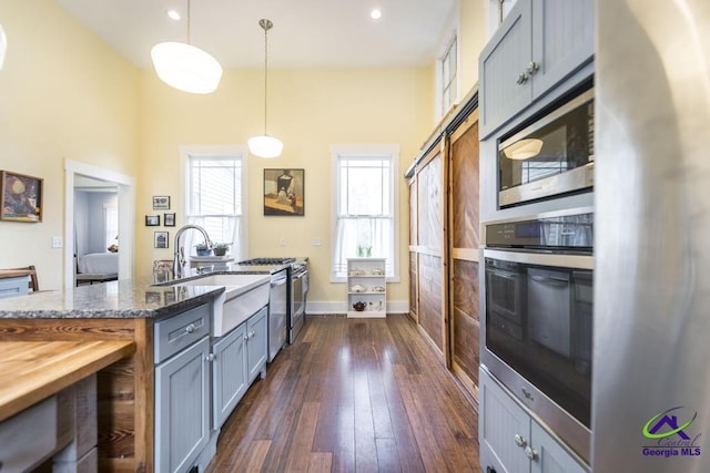 kitchen featuring wooden counters, decorative light fixtures, dark wood-style floors, stainless steel appliances, and a sink