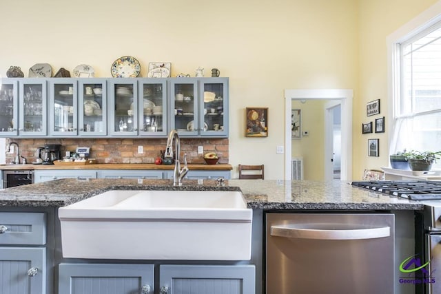 kitchen with dark stone counters, gray cabinetry, a sink, dishwasher, and tasteful backsplash