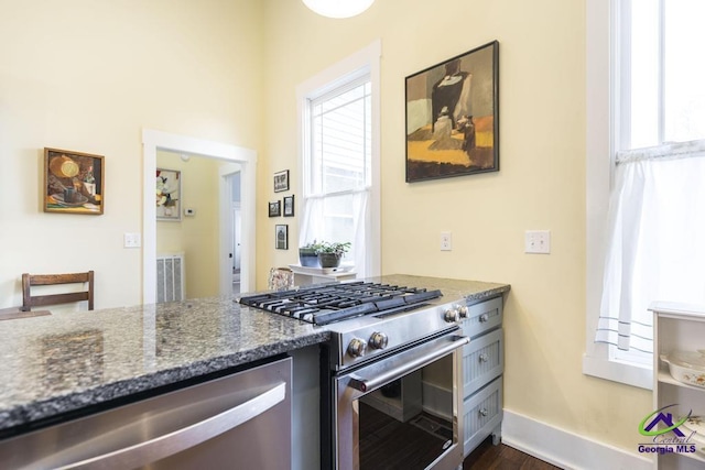 kitchen with dark stone counters, baseboards, appliances with stainless steel finishes, and a healthy amount of sunlight