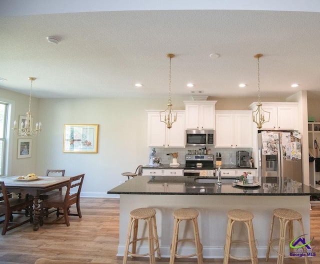 kitchen with a center island with sink, light wood-type flooring, appliances with stainless steel finishes, a kitchen bar, and tasteful backsplash