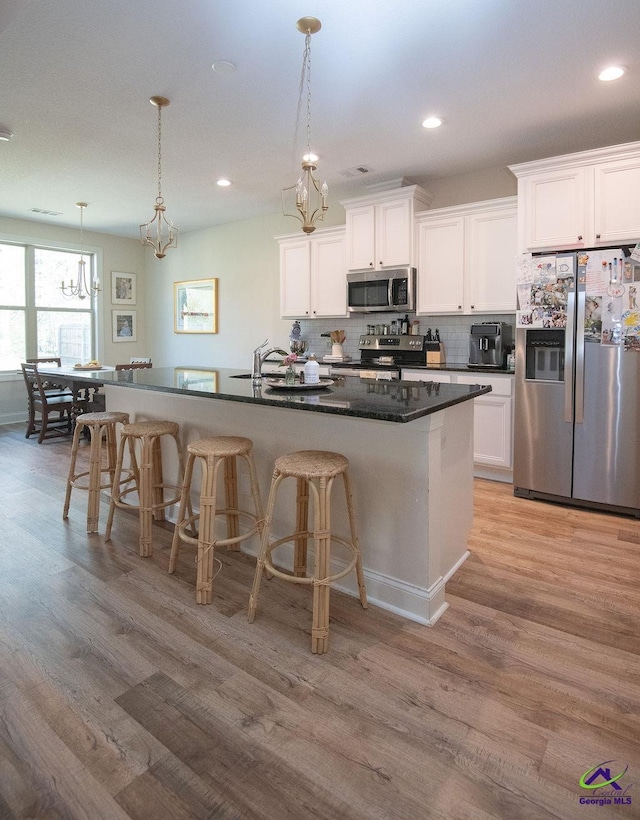 kitchen featuring tasteful backsplash, a kitchen bar, a large island with sink, appliances with stainless steel finishes, and light wood-style floors