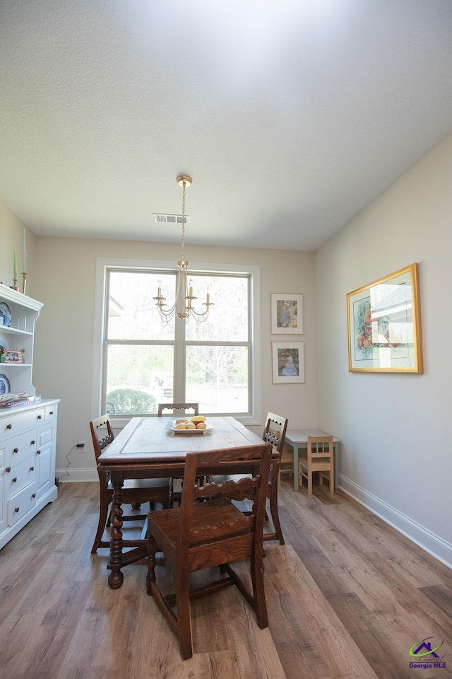 dining area with light wood finished floors, visible vents, an inviting chandelier, and baseboards