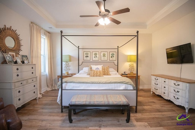 bedroom featuring a raised ceiling, wood finished floors, crown molding, baseboards, and ceiling fan