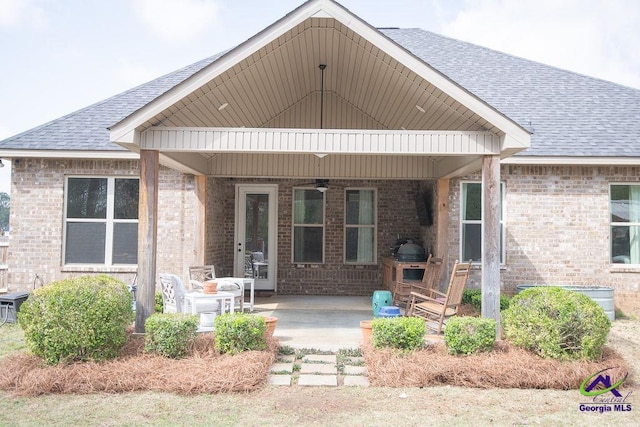 back of property featuring a patio, a ceiling fan, brick siding, and roof with shingles