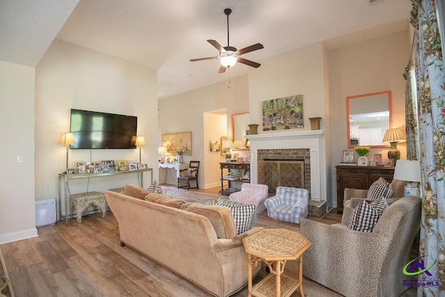 living room featuring a brick fireplace, baseboards, wood finished floors, high vaulted ceiling, and a ceiling fan