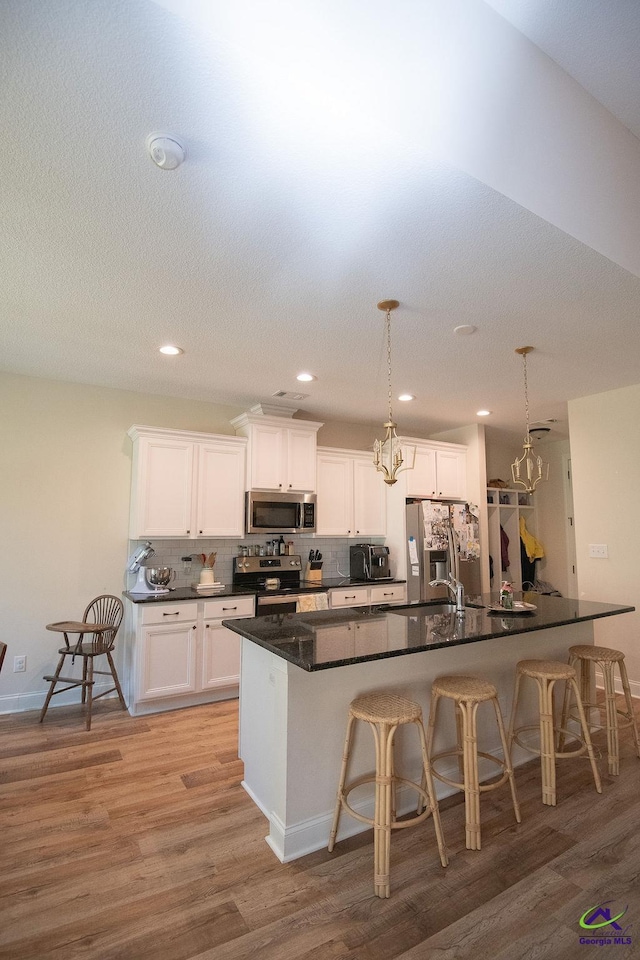 kitchen with dark countertops, light wood finished floors, a breakfast bar area, decorative backsplash, and appliances with stainless steel finishes