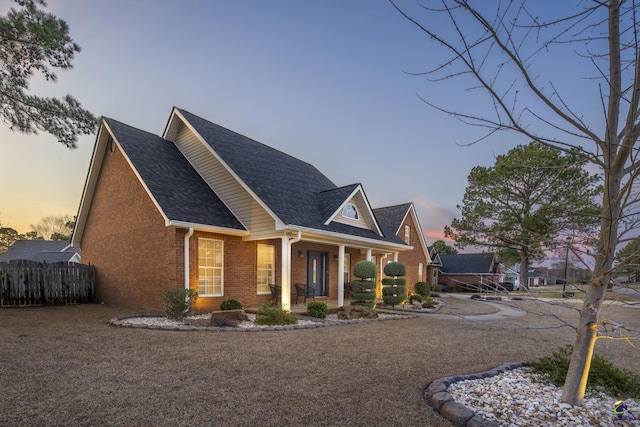 view of front of property featuring brick siding, covered porch, a shingled roof, and fence