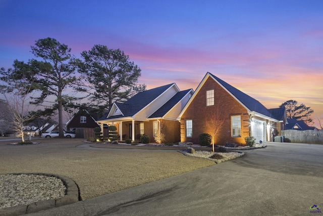 view of front of property featuring brick siding, an attached garage, driveway, and fence