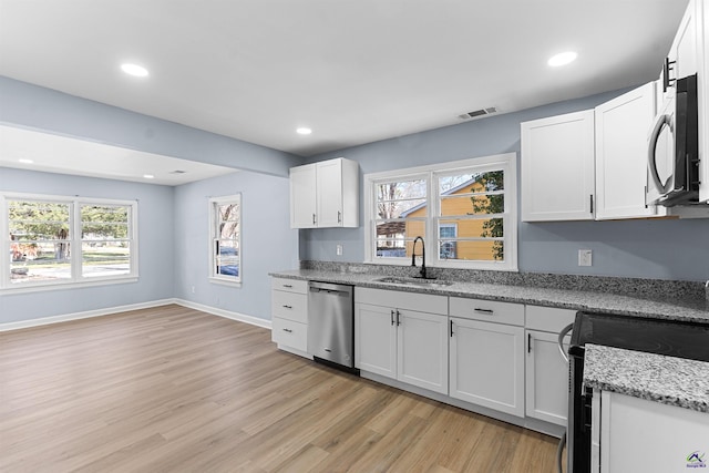 kitchen featuring light wood-type flooring, a sink, light stone counters, stainless steel dishwasher, and baseboards