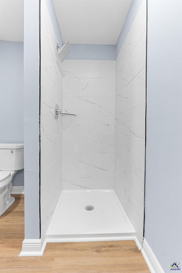 bathroom featuring baseboards, toilet, wood finished floors, and a shower stall