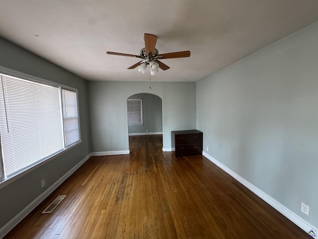 unfurnished room featuring visible vents, baseboards, hardwood / wood-style flooring, arched walkways, and a ceiling fan