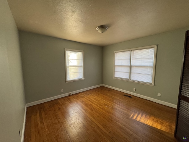 unfurnished room featuring visible vents, a textured ceiling, baseboards, and hardwood / wood-style flooring