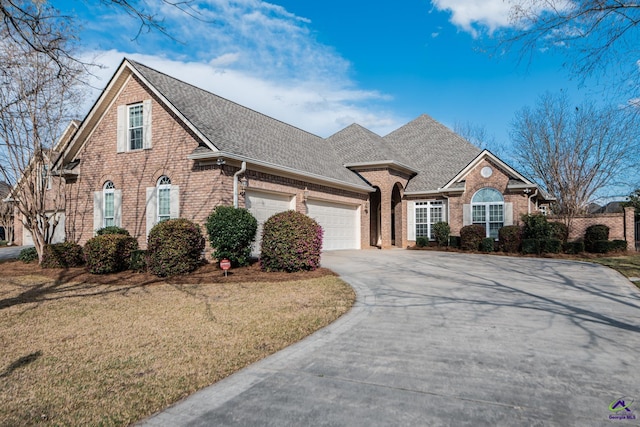 traditional home with roof with shingles, concrete driveway, a front yard, an attached garage, and brick siding