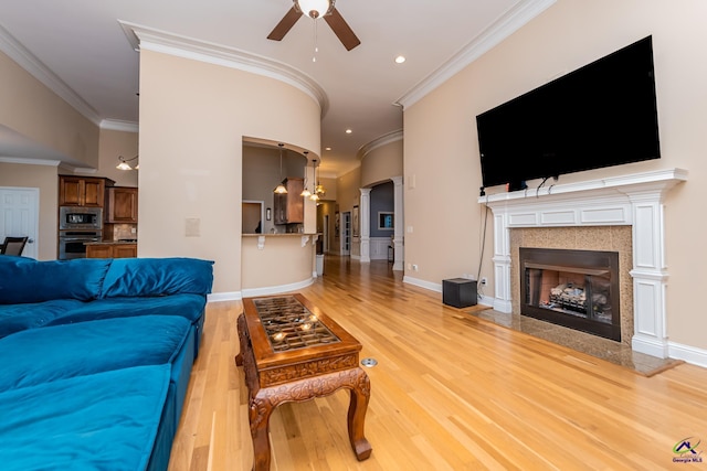 living area with a high end fireplace, light wood finished floors, crown molding, arched walkways, and a ceiling fan