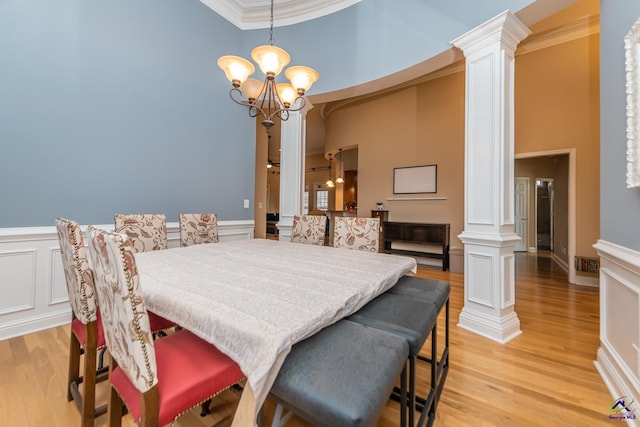 dining space featuring a notable chandelier, light wood-style floors, a high ceiling, crown molding, and decorative columns