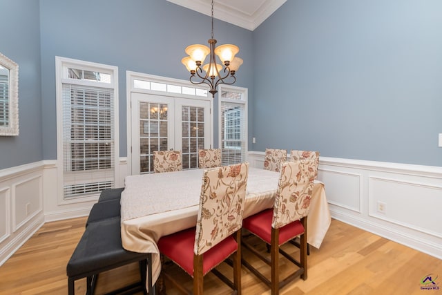 dining space with light wood-type flooring, vaulted ceiling, ornamental molding, wainscoting, and a notable chandelier