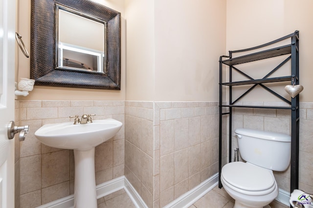 half bath featuring tile walls, toilet, and wainscoting