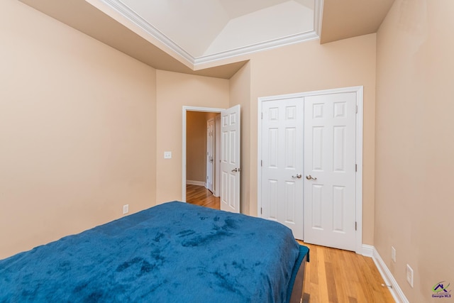 bedroom featuring crown molding, baseboards, a tray ceiling, light wood-style floors, and a closet