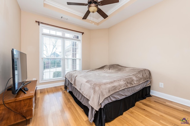 bedroom featuring visible vents, light wood-style flooring, crown molding, and a raised ceiling