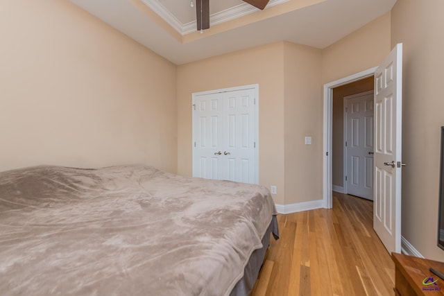 bedroom with light wood-style flooring, a tray ceiling, a closet, crown molding, and baseboards