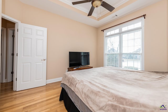 bedroom featuring light wood-type flooring, visible vents, a tray ceiling, crown molding, and baseboards