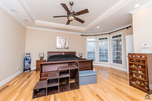 bedroom featuring wood finished floors, visible vents, baseboards, crown molding, and a raised ceiling