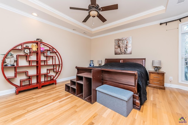 bedroom with a tray ceiling, crown molding, baseboards, and wood finished floors