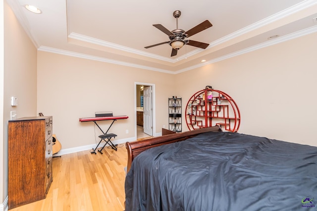 bedroom featuring a tray ceiling, crown molding, light wood-style floors, and baseboards