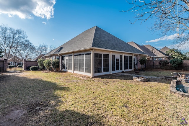 back of property featuring a shingled roof, a fire pit, fence, a yard, and a sunroom