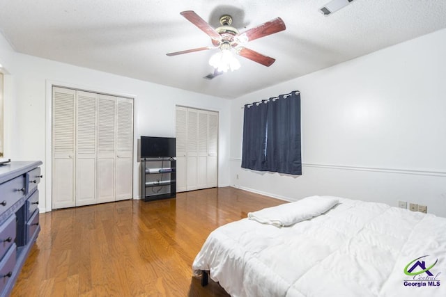 bedroom featuring a textured ceiling, two closets, ceiling fan, and wood finished floors