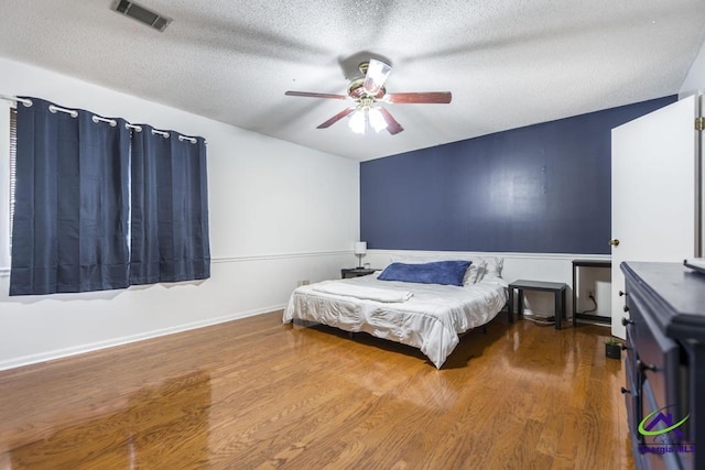 bedroom featuring visible vents, baseboards, ceiling fan, wood finished floors, and a textured ceiling