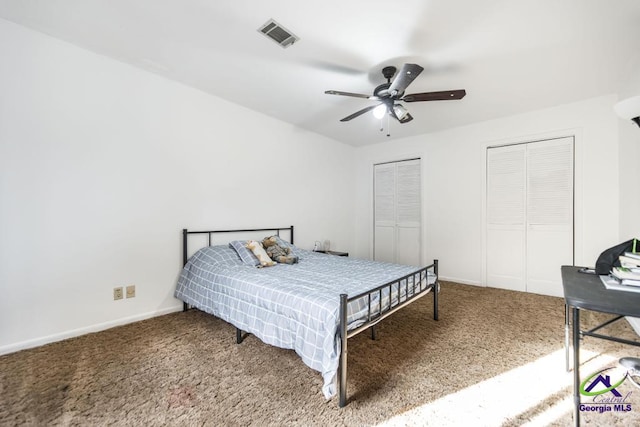 carpeted bedroom with visible vents, two closets, baseboards, and a ceiling fan