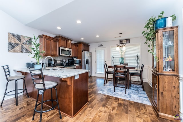 kitchen featuring a sink, dark wood-style floors, stainless steel appliances, a peninsula, and light stone countertops