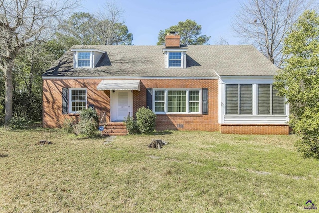 cape cod house with brick siding, a chimney, a front yard, and roof with shingles