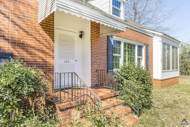 doorway to property featuring brick siding and roof with shingles