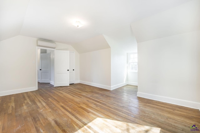 additional living space with baseboards, an AC wall unit, light wood-style flooring, and vaulted ceiling