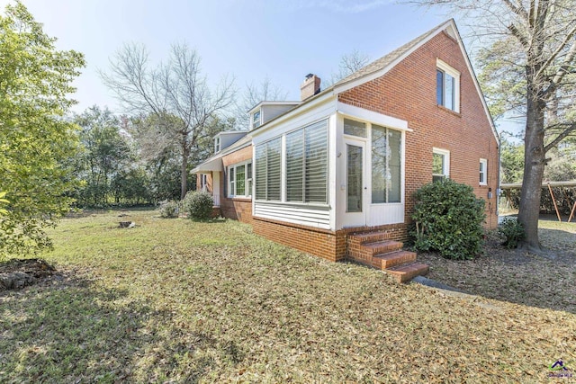 view of side of home with entry steps, a yard, a sunroom, and a chimney